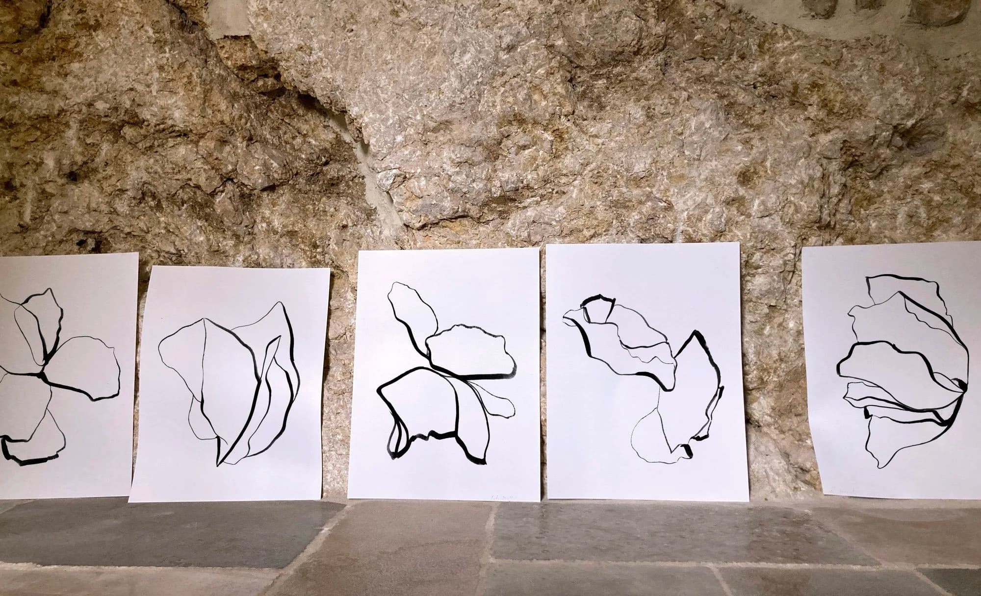 Série de dessins contemporains à l’encre noire aux lignes organiques et formes florales abstraites présentée sur fond de pierre naturelle