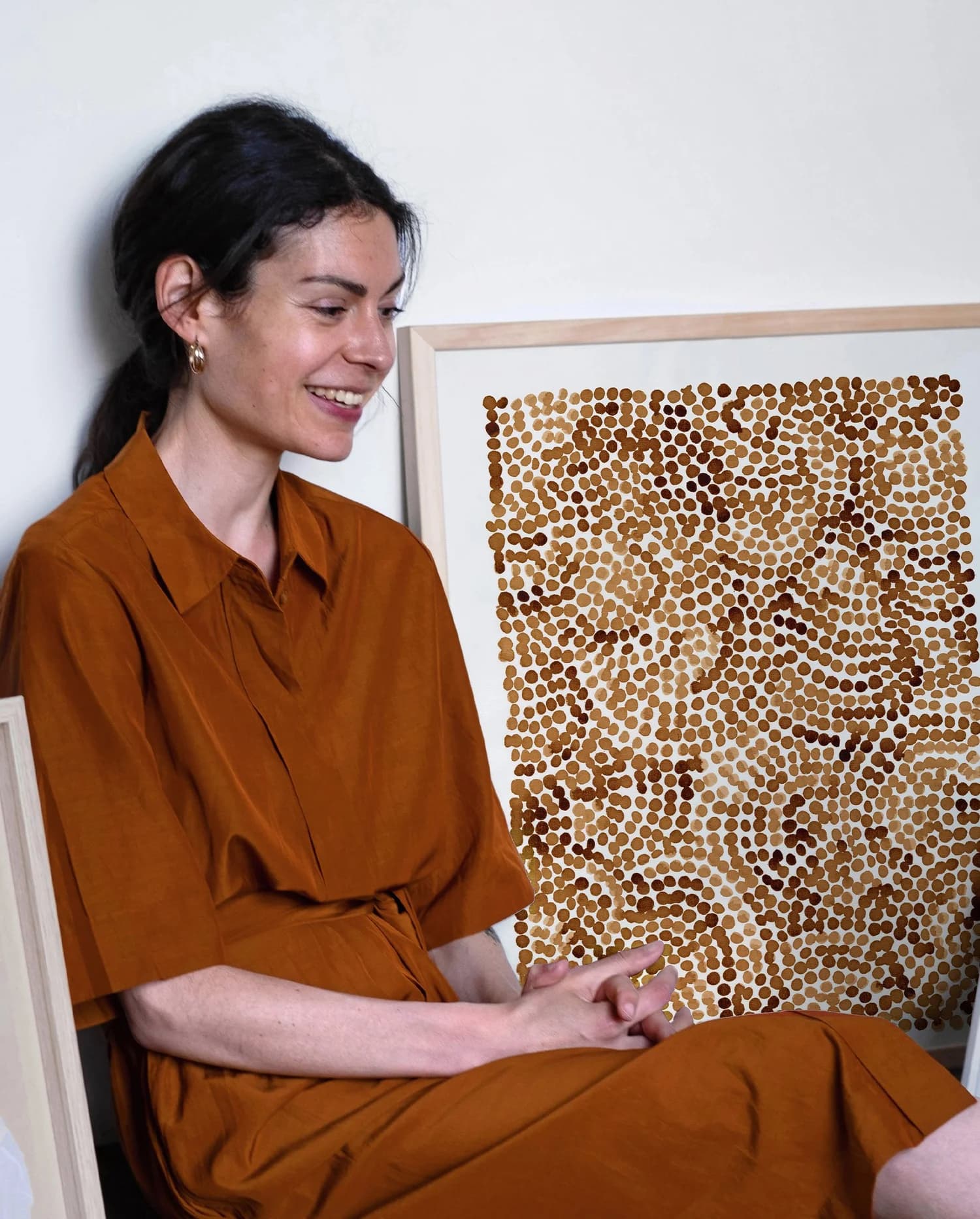 Portrait de l’artiste Lola Mathé assise à côté d’une œuvre contemporaine abstraite aux tons ocres et bruns