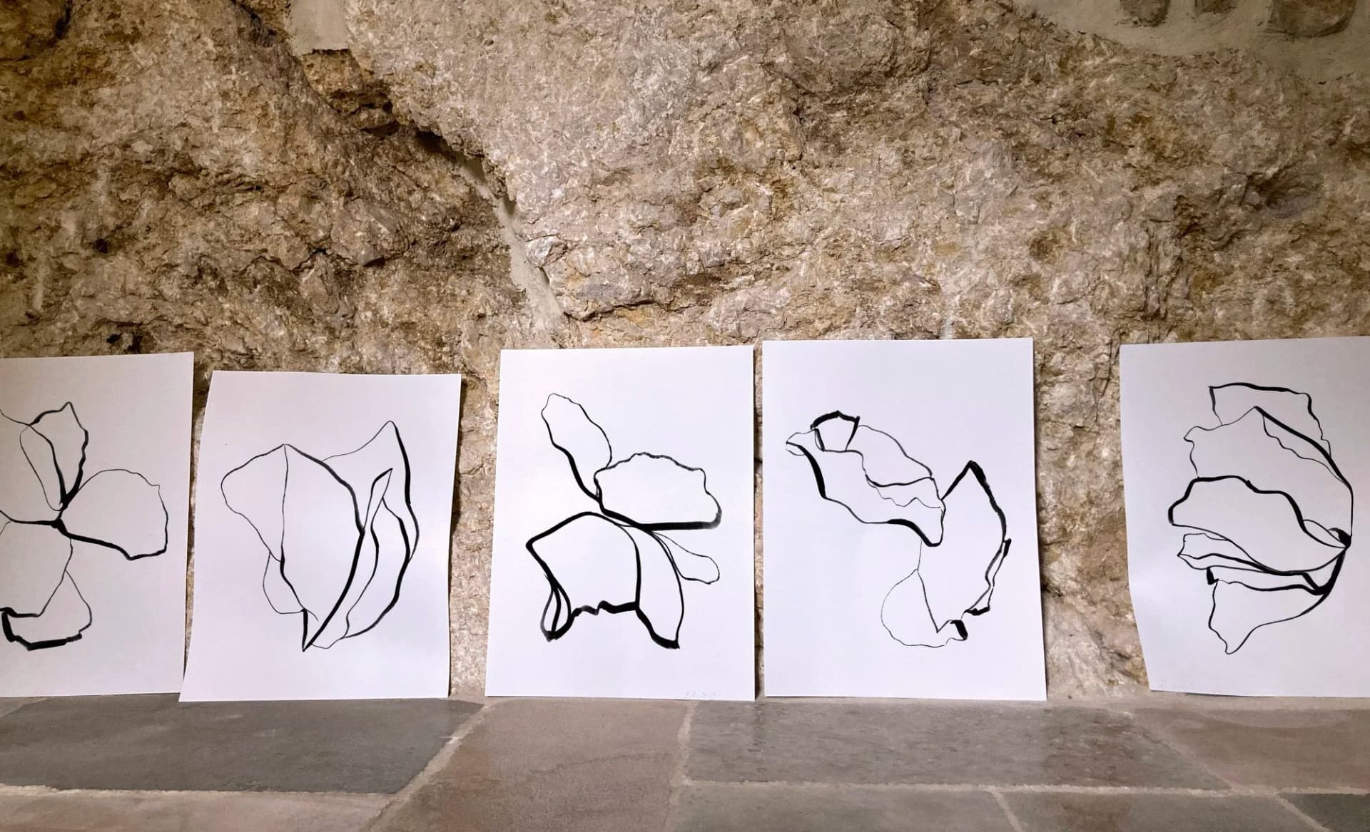 Série de dessins contemporains à l’encre noire aux lignes organiques et formes florales abstraites présentée sur fond de pierre naturelle